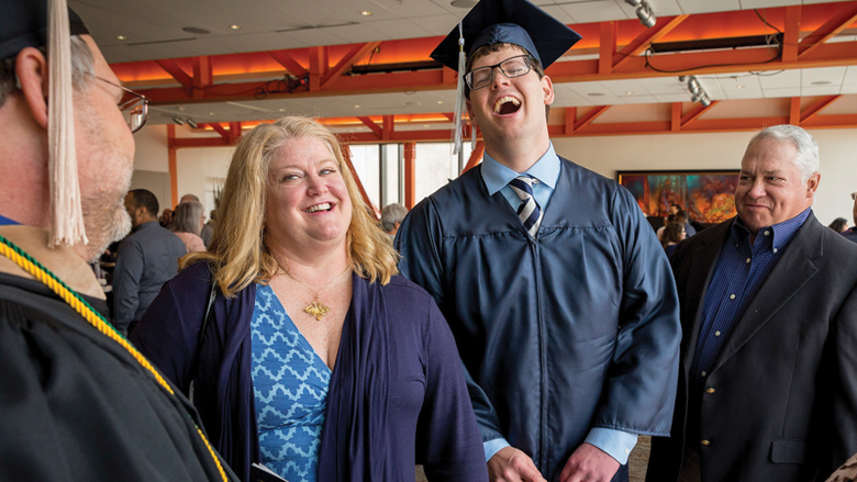 学生戴着毕业帽，穿着毕业服，和家人一起欢笑 