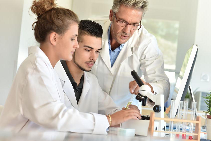 三个穿着实验室工作服的人站在显微镜前