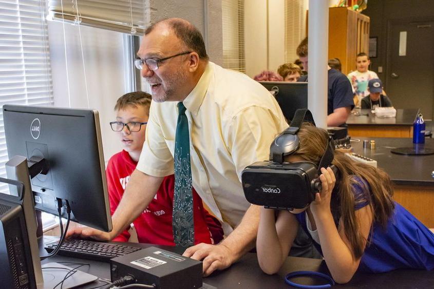 迈克尔·加利 assists middle schoolers who are trying on VR headsets.